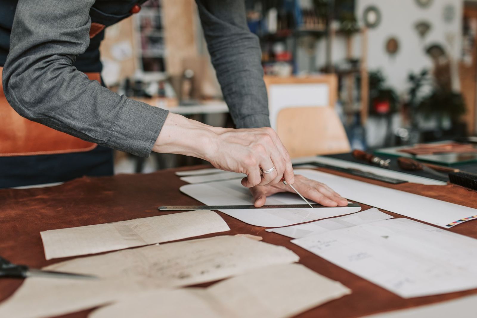 Hands cutting around a paper template on brown leather with a utility blade