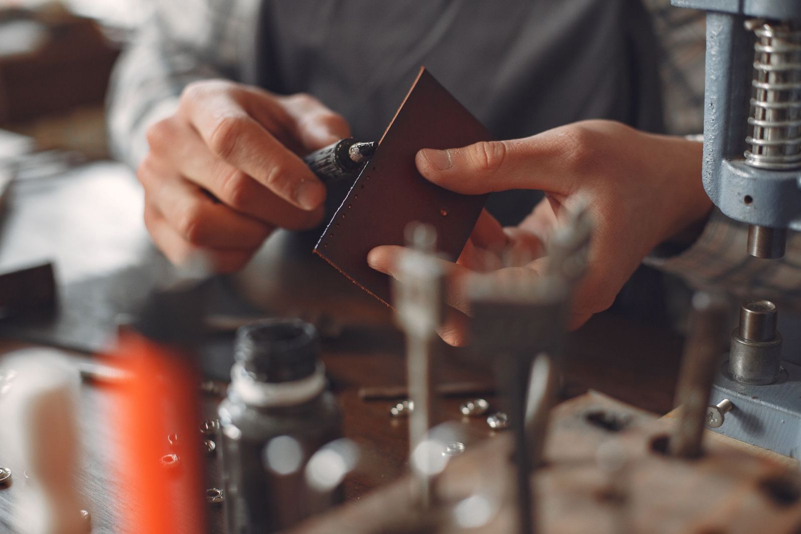 An artisan applying edge finish to a small brown leather piece with a pen applicator