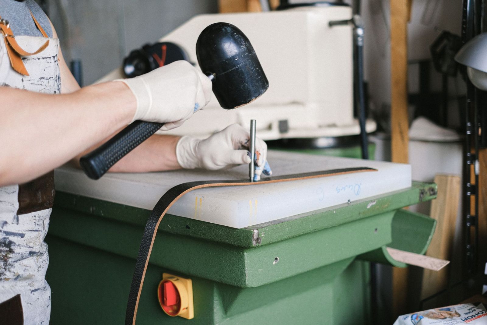 A leatherworker striking a punch with a mallet to pierce a leather strap on the bench