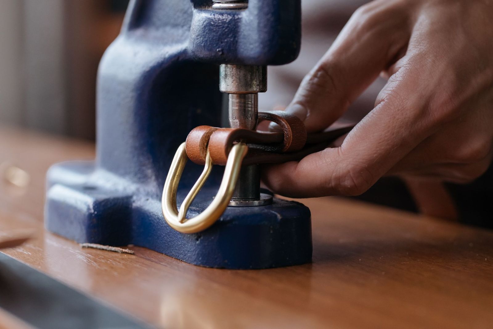 A rivet being pressed into a brass-buckled leather belt with a hand press