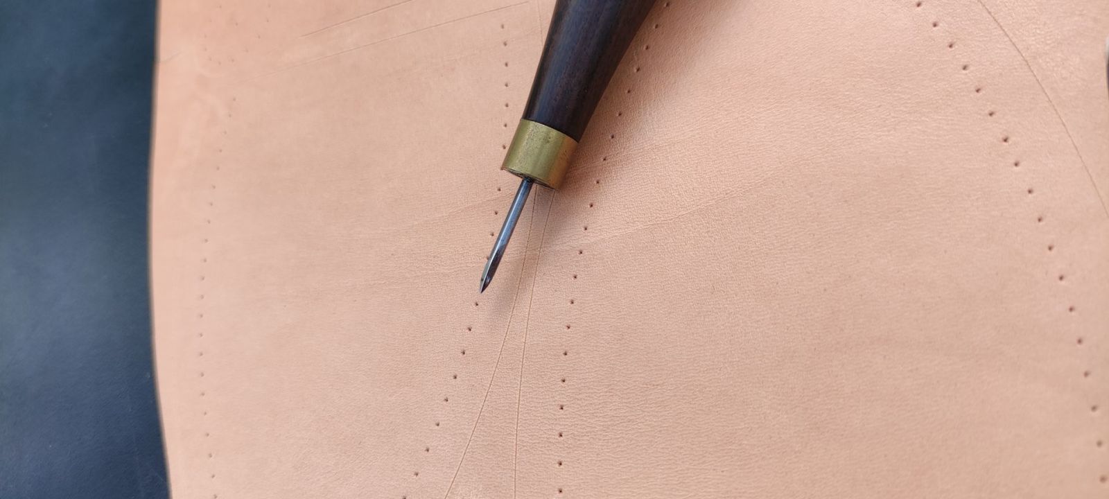 A wooden-handled diamond stitching awl piercing pricked holes on natural veg-tan leather
