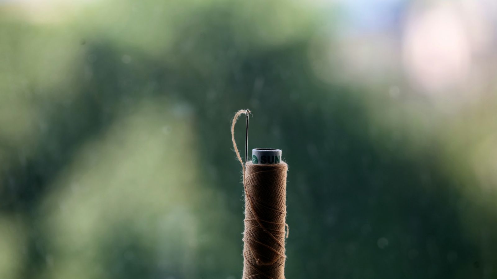 A spool of waxed brown hand-stitching thread with a needle threaded at its tip